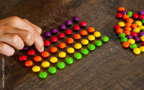 woman's hand collects even row of colorful candies on a wooden background