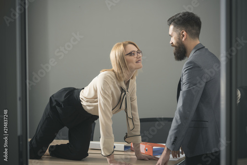 Sexual flirt at work. Sexy secretary seduce boss in office. Businesswoman on desktop look at bearded businessman. Man under woman domination, matriarchy. Office romance concept