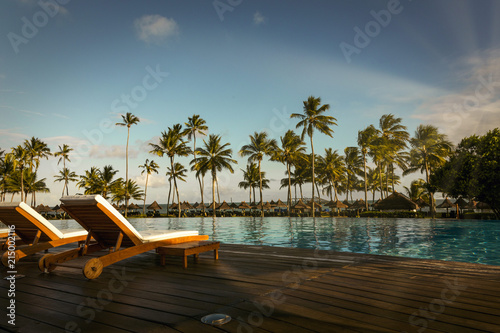 Beautiful tropical beach front hotel resort with swimming pool, sun-loungers and palm trees during a warm sunny day, paradise destination for vacations