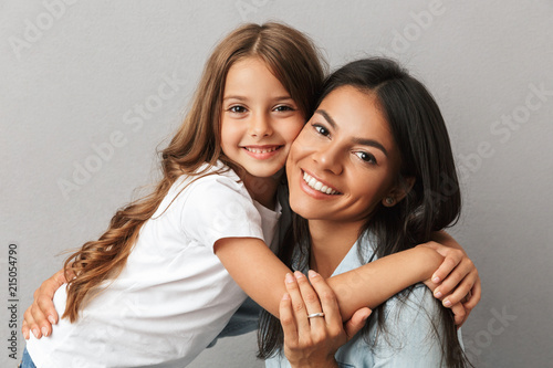 Photo of attractive woman with little daughter smiling and hugging together, isolated over gray background