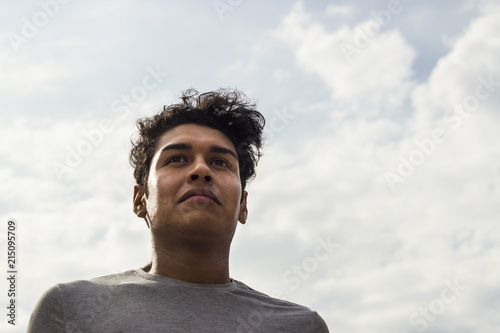 Confident latino guy smiling. Successful student with sky background