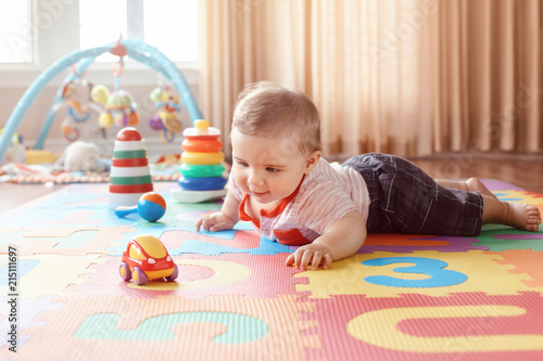 Portrait of cute adorable blond Caucasian smiling child boy with blue eyes crawling on floor in kids children room. Little baby playing with toys on playmat at home. Early education development