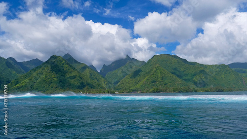 Beautiful ocean waves approach the vivid green mountains of the lush island.