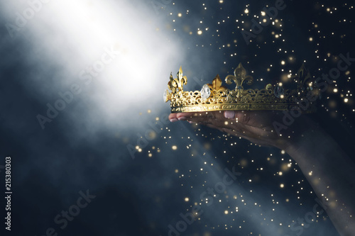 mysteriousand magical image of woman's hand holding a gold crown over gothic black background. Medieval period concept.