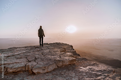 Alone man in israel negev desert admires the view of sunrise. Young male person stands on the edge of the cliff