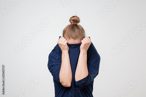 European woman hiding face under the clothes. She is oulling sweater on her head.