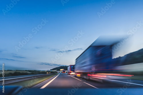 Background photograph of a highway. Truck on a motorway, motion blur, light trails. Evening or night shot of trucks doing logistics and transportation on a highway.