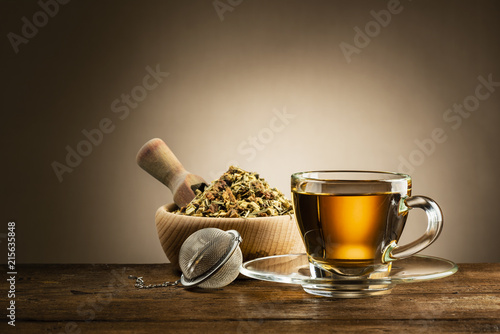 glass cup of tea with infuser and herbal tea on wooden table