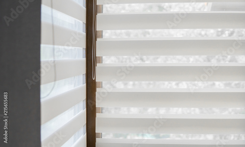 Details of white fabric roller blinds on the plastic window with wood texture in the living room.