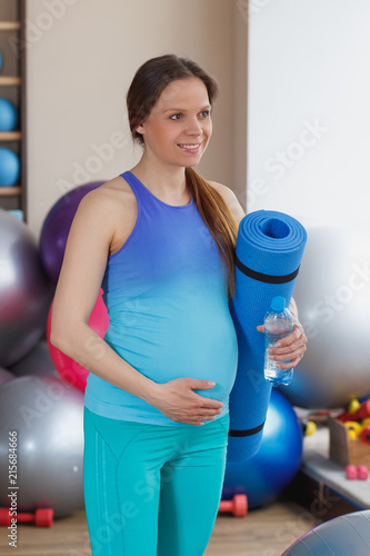 Pregnant woman with a mat in the gym