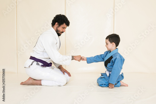 Male karate instructor training little child in dojo or jiu-jitsu at gym at tatami. Trainer teaches kid the basics of fighting for self-defense