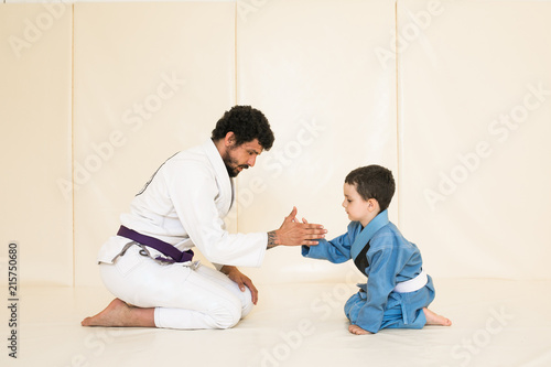 Ojciec i mały syn są zaangażowani w zapasy jiu-jitsu na siłowni w kimonie. Trener uczy dziecko metod i pozycji pojedynczej walki, karate lub aikido. Sport i zdrowie w rodzinie