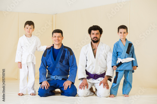 Male karate instructors training little children boys in dojo or jiu-jitsu at gym at tatami. Trainer teaches kid the basics of fighting for self-defense. Group of man and kids in sambo training