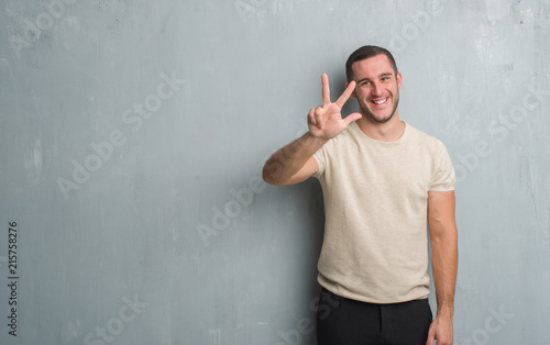 Young caucasian man over grey grunge wall showing and pointing up with fingers number three while smiling confident and happy.