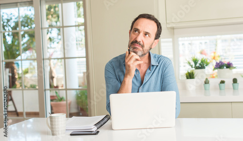 Middle age man using laptop at home serious face thinking about question, very confused idea