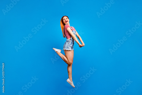 Full-size portrait of jumping carefree girl who laughs happily looking straight into the camera isolated on vivid blue background
