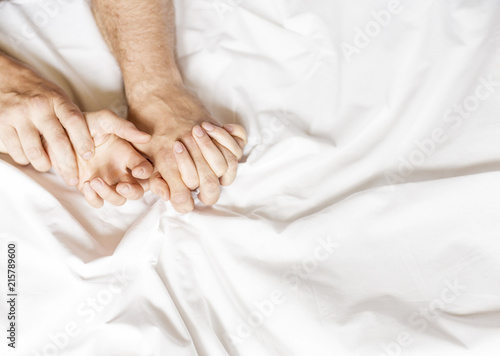 Couple having sex. Hand clutches grasps a white crumpled bed sheet in a hotel room, a sign of ecstasy, feeling of pleasure or orgasm