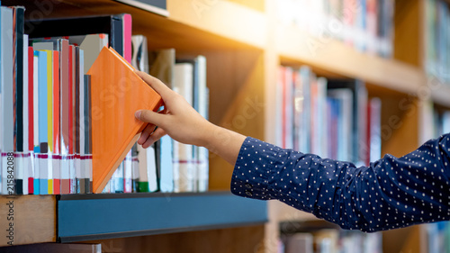 Male right hand choosing and picking orange book in public library. Pulling off selected textbook. Education research and self learning in university life concepts