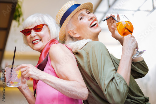 Two sisters. Joyful aged women standing together while enjoying their cocktails