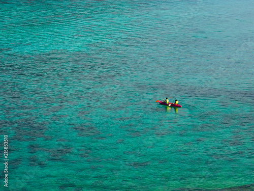 Two travelers in pink kayak in turquoise water sea for summer vacations holiday concept, bird eye view.