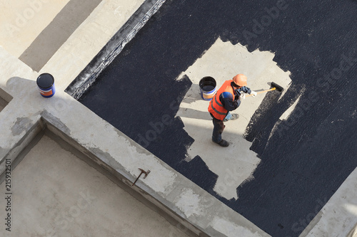 The worker in overalls applies an insulation coating on the concrete surface. View from above.