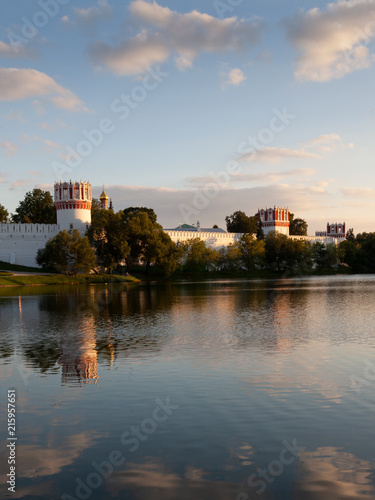 The walls and towers of the Novodevichy monastery in Moscow are reflected in the water in the summer evening sunset