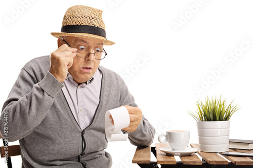 Shocked mature man seated at a coffee table looking at the bill