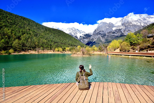 back of girl travel alone sit in front of extremely blue river ,Blue Moon valley, Jade Dragon Snow Mountain seen from a distance, Lijiang, China