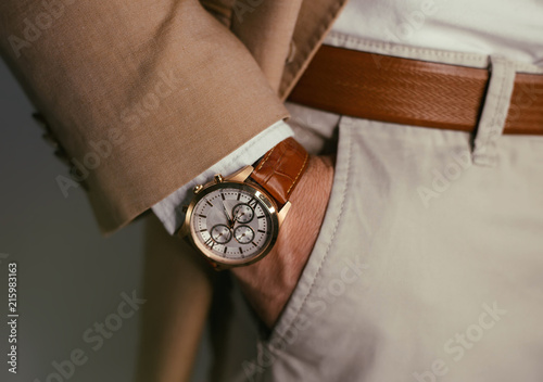 Closeup fashion image of luxury watch on wrist of man.body detail of a business man.Man's hand in brown pants pocket closeup at white background.Man wearing brown jacket and white shirt.Toned.