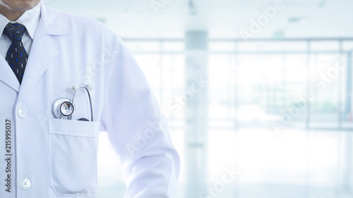 Male doctor with stethoscope in a pocket partailly cropped on a blurry hospital background with side copy space.