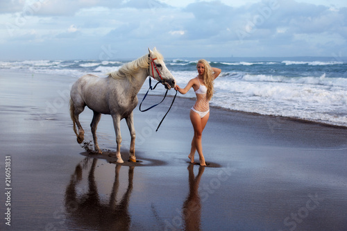 Beautiful young woman walking with horse at the beach, horseback