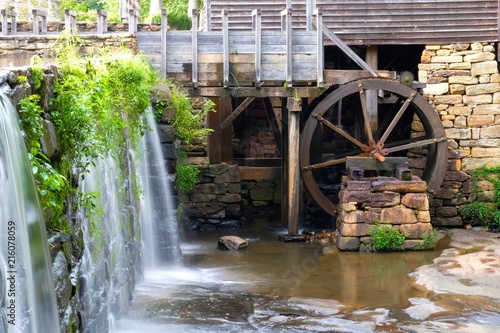 The greenery droops over the waterfall with the flume and waterwheel in view at Historic Yates Mill County Park in Raleigh North Carolina