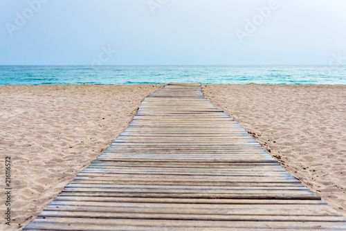 Wooden boardwalk at beach in sand and sea in the background