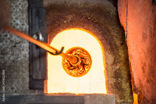 Murano glass-blowing factory. Glass blower forming beautiful piece of glass: put iron rod with attached glass object in furnace to make the glass malleable. Italy