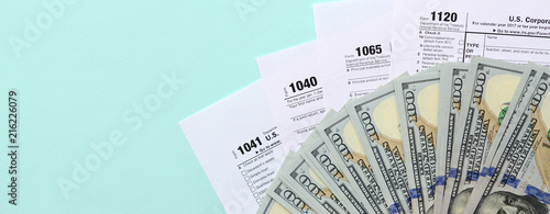 Tax forms lies near hundred dollar bills and blue pen on a light blue background. Income tax return