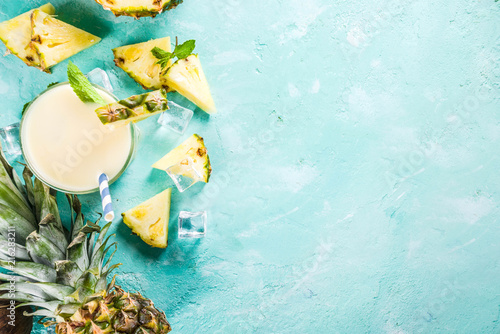 Refreshing summer drink, homemade pina colada cocktail, on a light blue background, with pieces of pineapple, coconut, ice and mint leaves, copy space top view