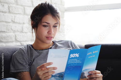 Woman Reading Travel Flye On Sofa At Home