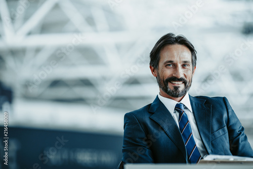 Portrait of beaming bearded male having job indoor. He looking at camera. Positive employer concept. Copy space
