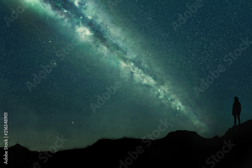 Silhouette of a young girl on a mountainous landscape at night against a blue sky full of stars and an incredible milky way