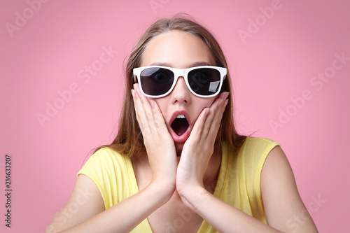 Portrait of surprised young woman in sunglasses on pink background