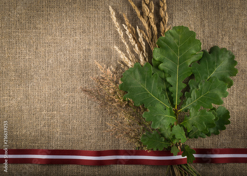 Composition of latvian flag ribbon, branch of oak and cut dried grass