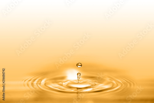 Closeup on drop of cosmetic golden oil liquid creating a circular wave.