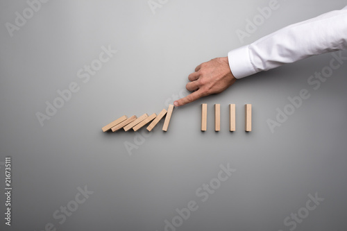 Hand of business man stopping falling domino pieces