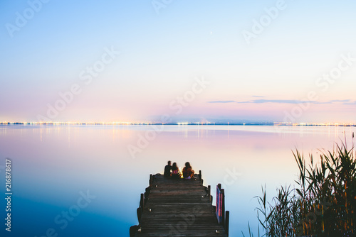 People resting relaxed on a pier on a lake at sunset with calm water