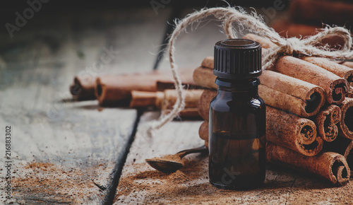 Essential cinnamon oil in a small bottle, ground cinnamon and cinnamon sticks on old wooden background, selective focus and toned image
