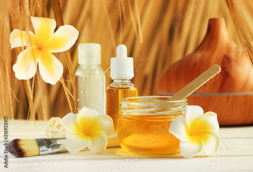 Honey spa with tropical flower frangipani decor, jars with golden beauty treatment oils for relaxing skin care under straw thatch.