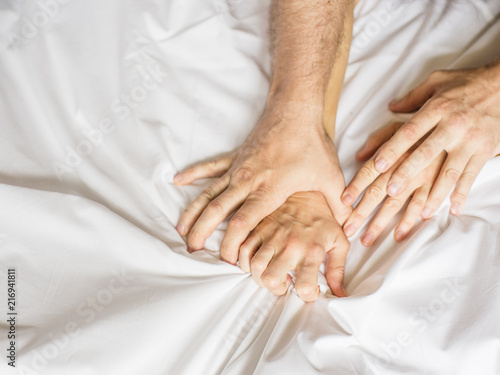 Couple having sex. Hand clutches grasps a white crumpled bed sheet in a hotel room, a sign of ecstasy, feeling of pleasure or orgasm