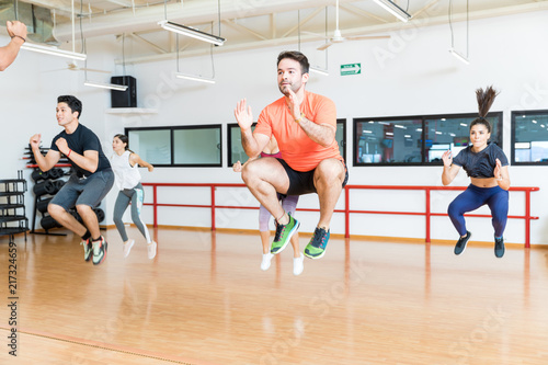 Clients Doing Tuck Jumps On Hardwood Floor In Gym