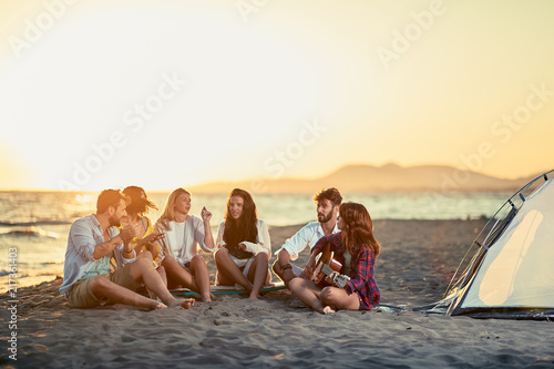 Friends with guitar at beach enjoyment. friends relaxing on sand at beach with guitar and singing on summer sunset.