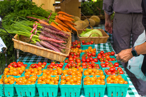 Variety of locally grown cherry tomatoes and carrots at Union Square Greenmarket Farmer's Market NYC with shoppers